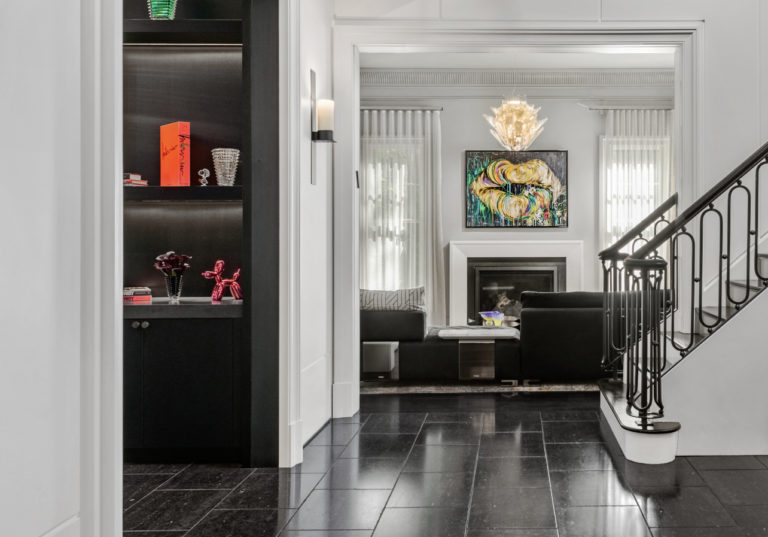 White staircase leading into a side hallway overlooking a transitional living room with fireplace