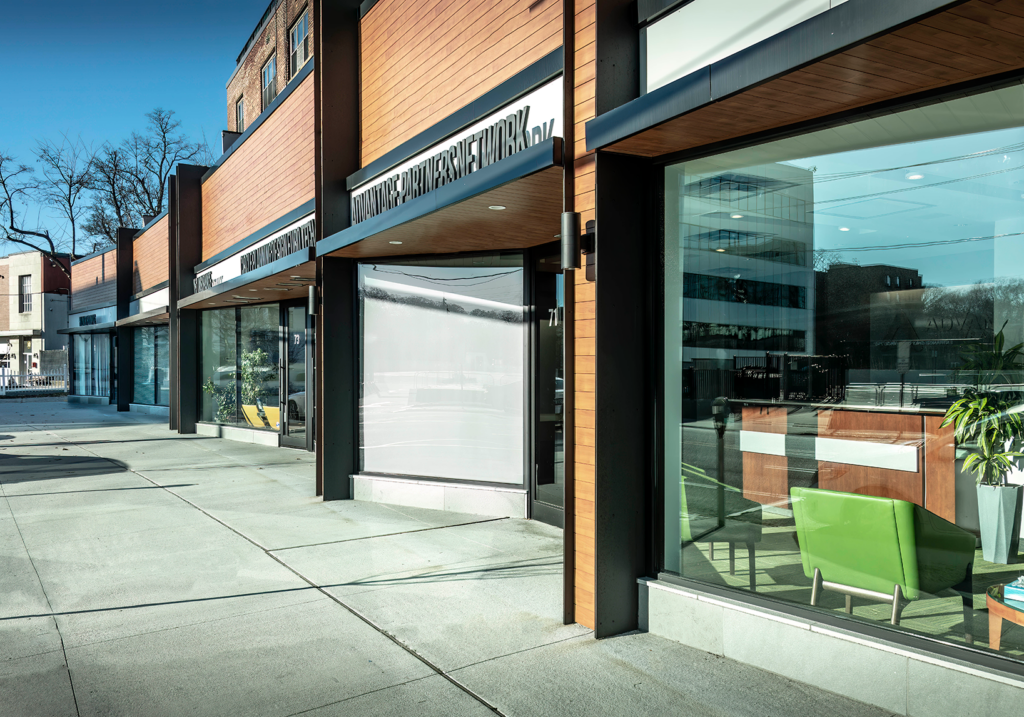 Contemporary retail storefronts with wood and black trim, large glass windows, and visible office furnishings inside.