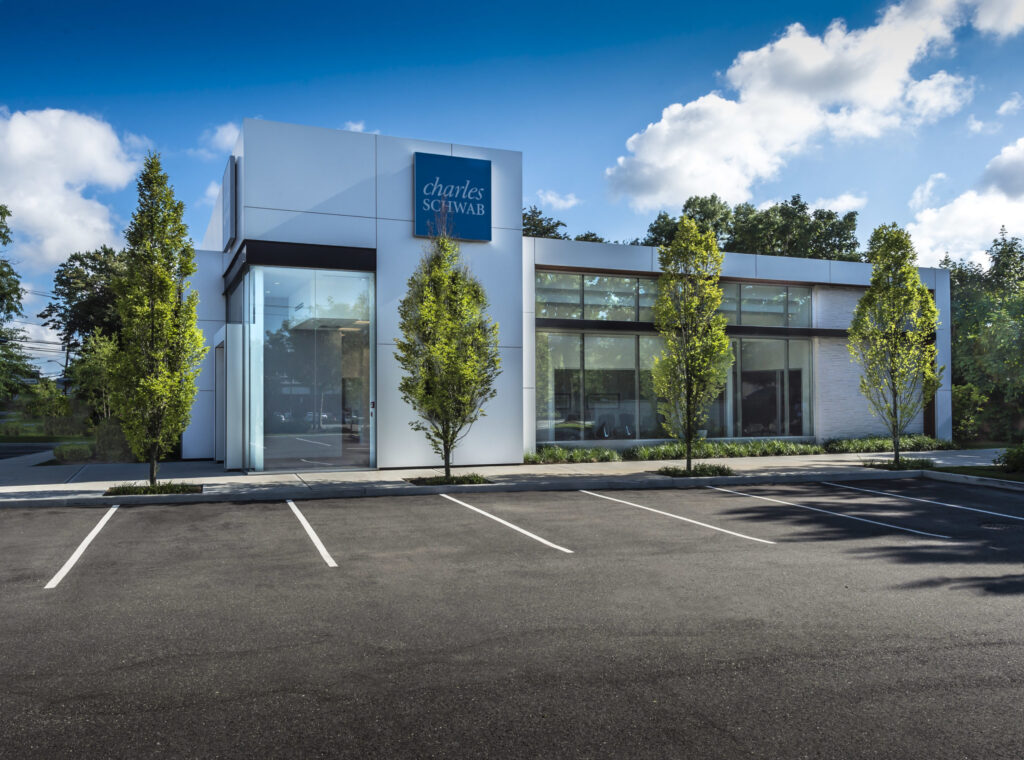 Minimalist Charles Schwab building with tall windows, a white exterior, and a clean parking lot framed by evenly spaced trees.